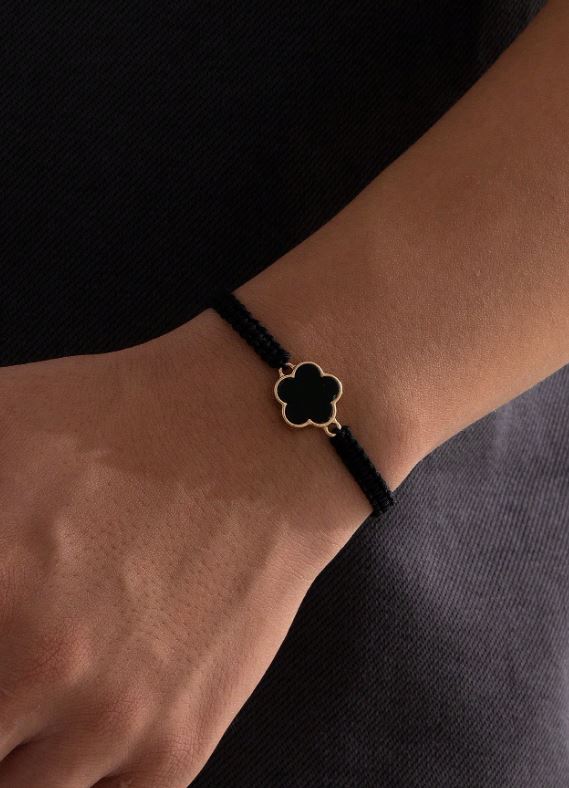 Black bracelet with a clover-shaped charm on a wrist against a black background