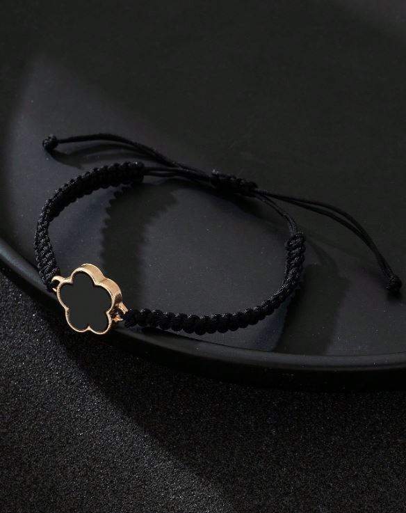 Black braided bracelet with a gold clover charm on a black background