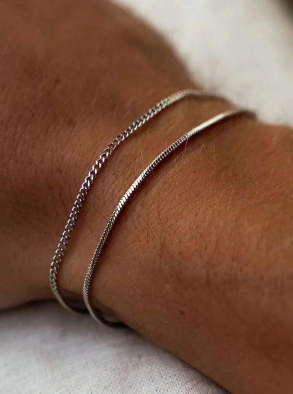 Close-up of a wrist wearing two silver bracelets on a light background