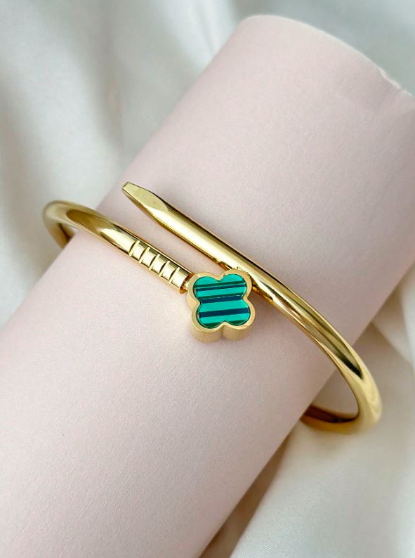 Gold bangle with a green clover charm on a light background