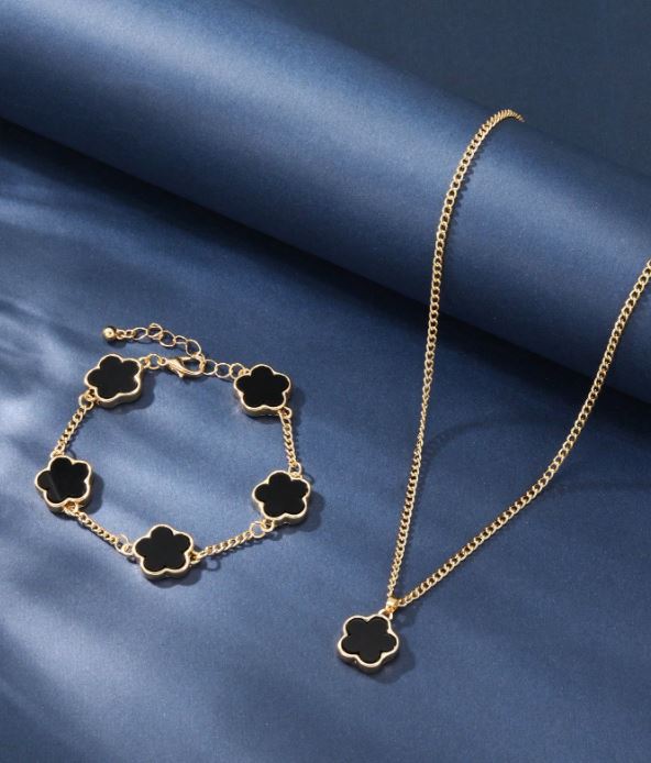 Gold bracelet and necklace with black clover-shaped charms on a blue satin background