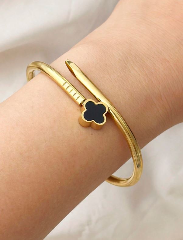 Gold bracelet with a clover-shaped charm on a wrist against a neutral background