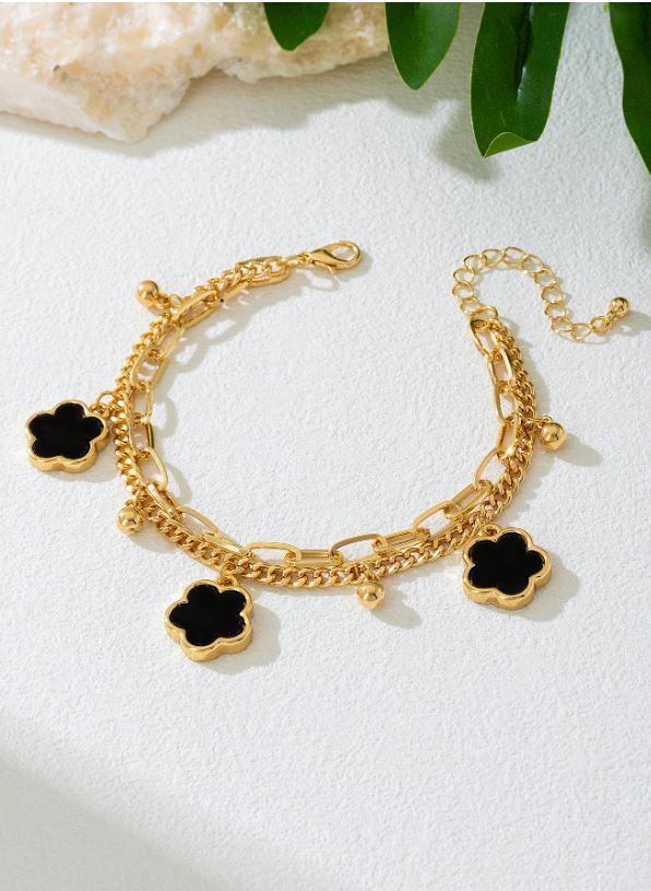 Gold bracelet with black clover charms on a white surface with green leaves in the background