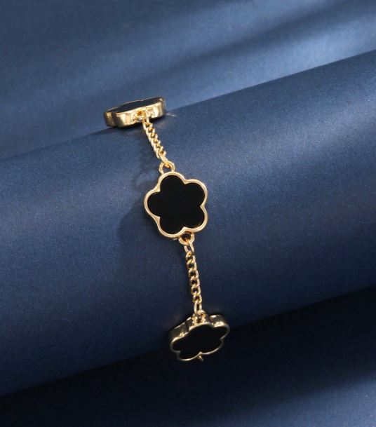 Gold brooch with black clover-shaped pendants on a blue fabric background