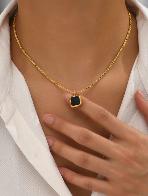 Gold necklace with a black pendant worn by a person
