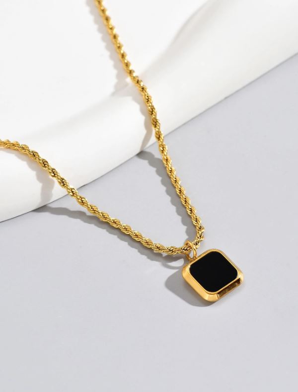 Gold necklace with a black square pendant on a light gray background