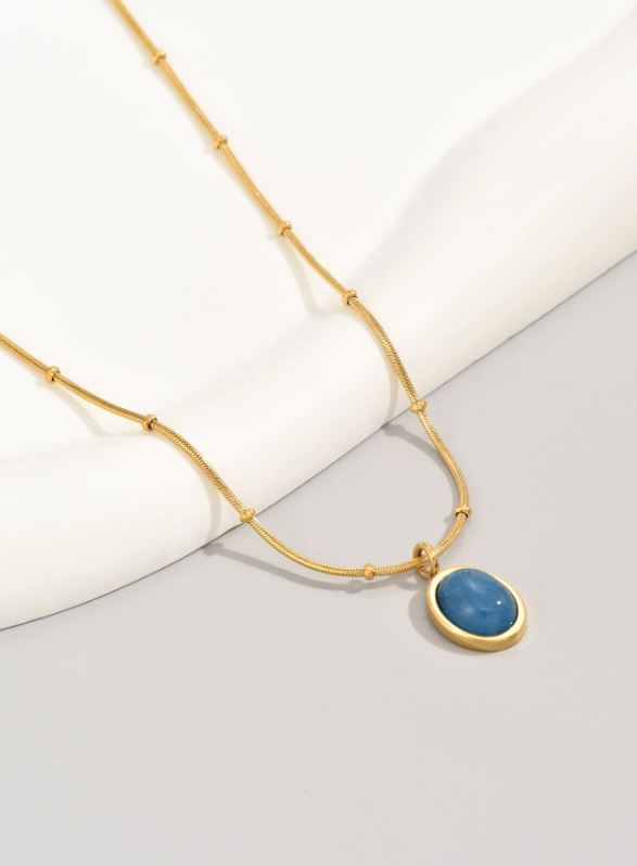 Gold necklace with a blue pendant on a light background