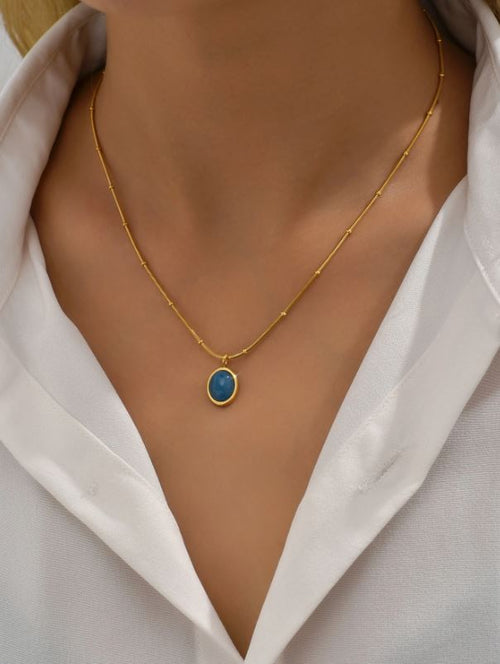 Gold necklace with a blue pendant on a white shirt
