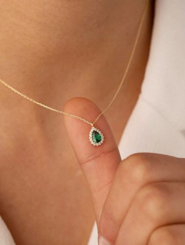 Gold necklace with a green gemstone held by a hand against a neutral background