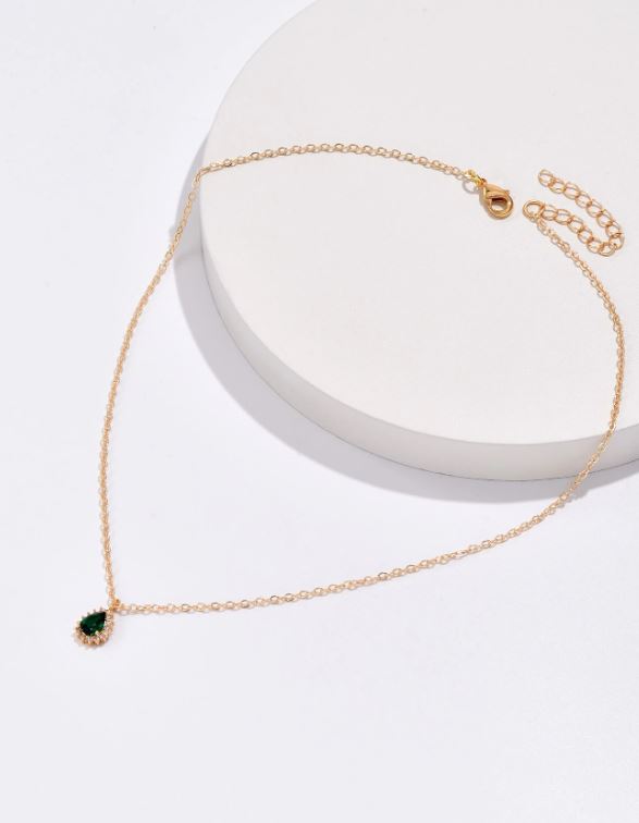 Gold necklace with a green gemstone on a white surface