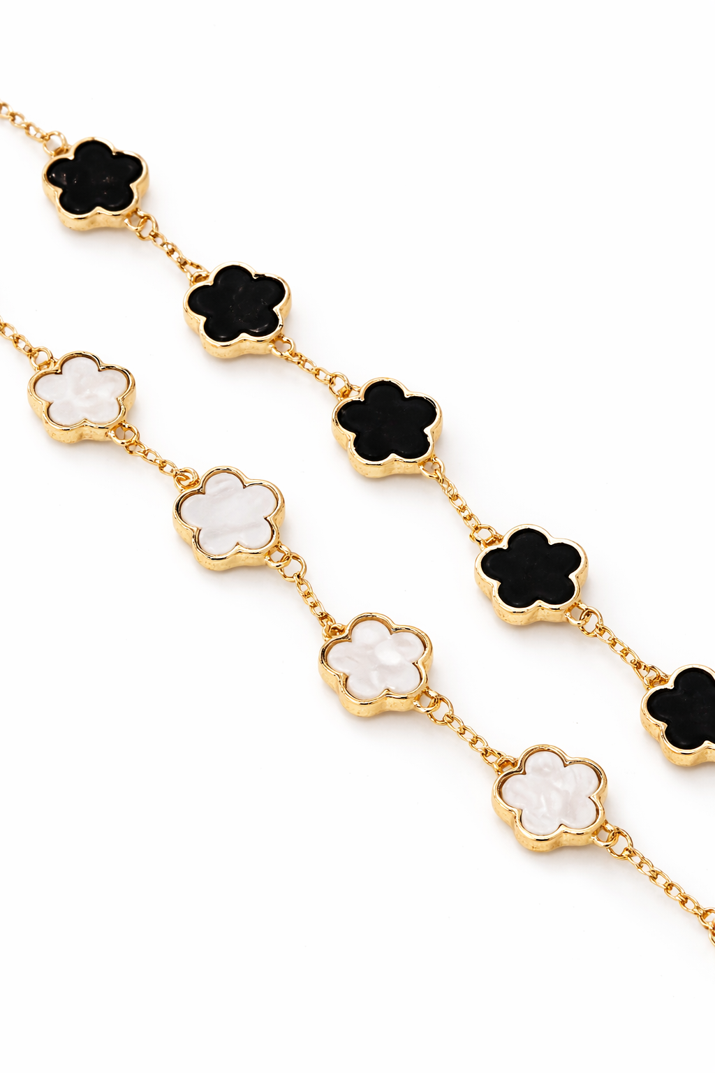 Gold necklace with black and white flower-shaped pendants on a white background