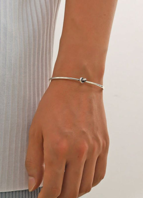 Silver bracelet on a wrist with a plain background