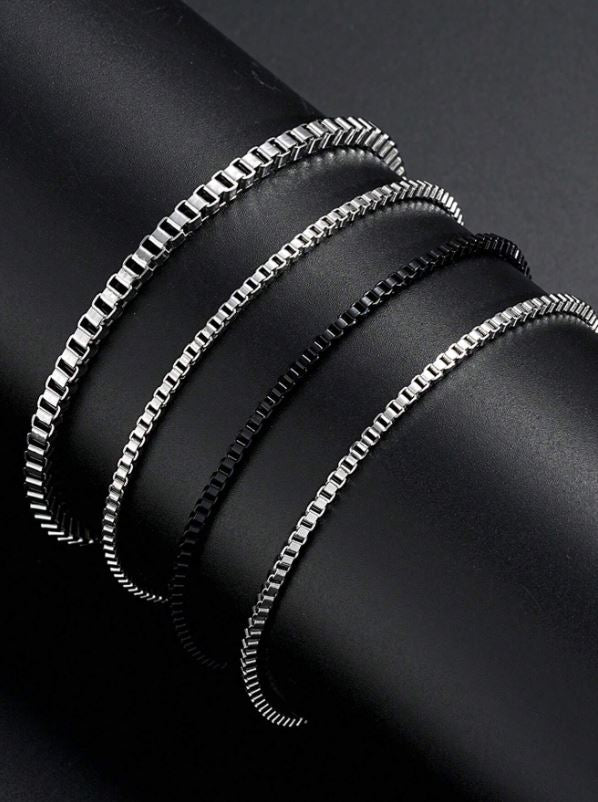 Three silver chain bracelets on a dark surface