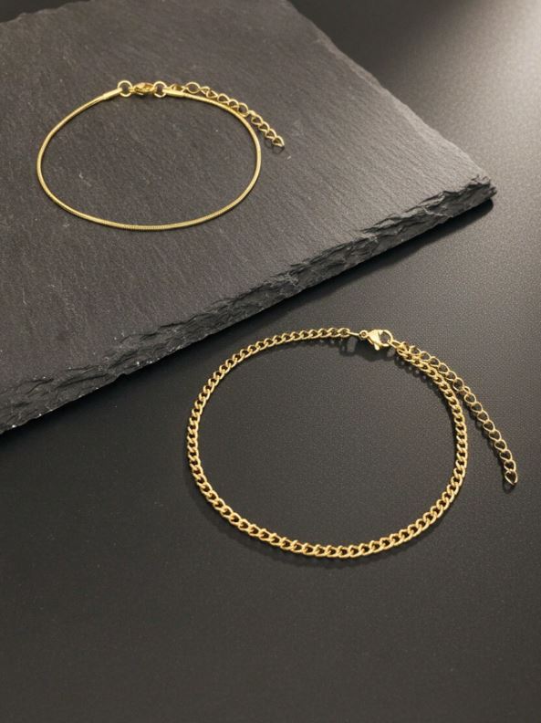 Two gold bracelets on a dark slate surface