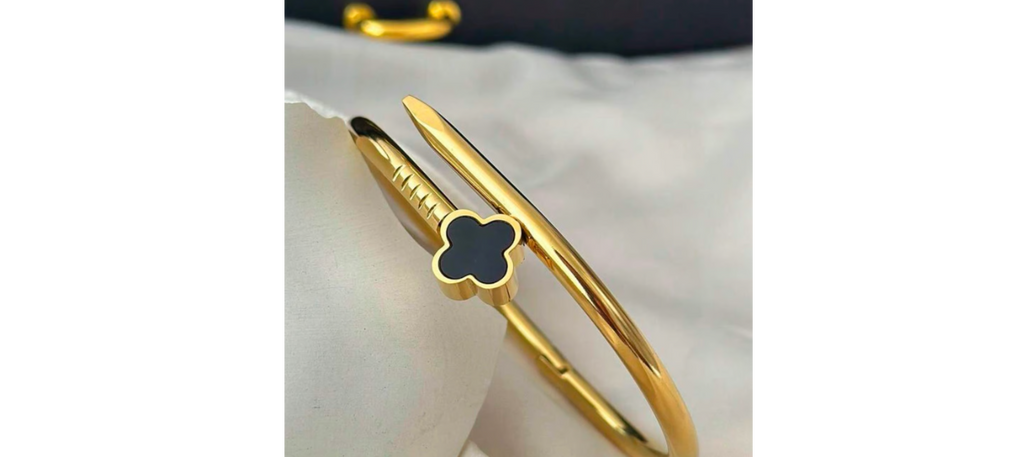 Gold bracelet with a black clover charm on a white surface