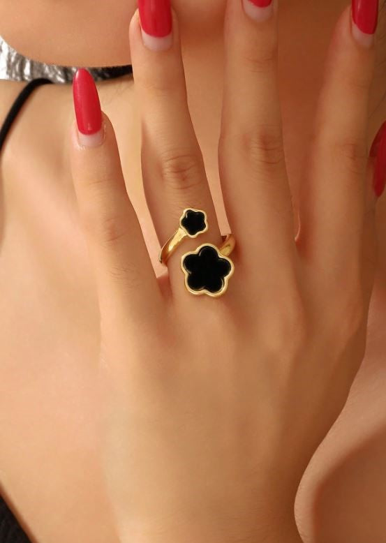 Close-up of a hand wearing a gold ring with black clover design on a light background
