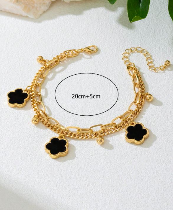 Gold bracelet with black clover charms on a white background