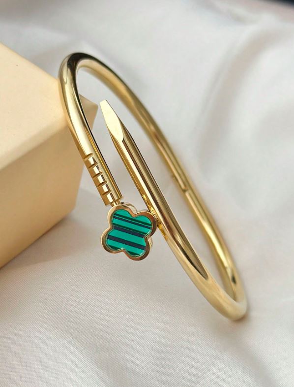 Gold bangle with a green clover charm on a light background