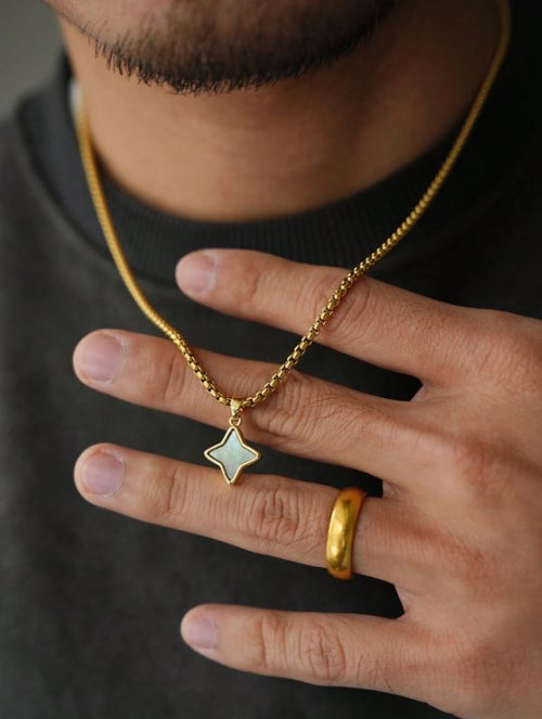 Close-up of a person wearing a gold necklace with a star pendant and a gold ring on a dark background.